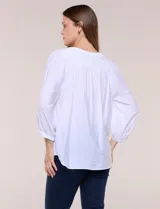 Blusa blanca de rayón y poliéster con textura, escote en V y delicados bordados al tono sobre el canesú. Cuenta con mangas raglán tres cuartos abullonadas con puños elastizados y diseño holgado.