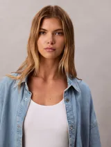 Camisa de denim de corte holgado, con cuello en punta, mangas largas y cierre frontal con botones. Presenta un diseño clásico con acabado lavado y monograma bordado en el pecho.