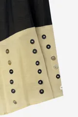 Falda de tiro medio confeccionada en hilatura de lino, color beige con bloques negros y detalles de abalorios y ojales metálicos aplicados a contraste. Cuenta con cierre lateral con cremallera oculta en costura.