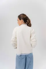 Saco básico de punto color marfil, confeccionado en lambswool, con corte entallado tipo chaquetita. Destaca por detalles de blonda tejida en los puños y a lo largo de la abertura frontal, con bordes en color contrastante.