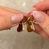 Par de caravanas tipo argolla con dije colgante en forma de corazón, con borde lateral decorado con pequeñas piedras brillantes.
