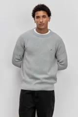 Sweater de tejido de punto acanalado en color marrón, con cuello redondo y ajuste holgado. Presenta un pequeño bordado distintivo en el pecho.