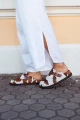 Suecos con capellada de cuero con estampado de vaca, plantilla anatómica y hebilla lateral ajustable.