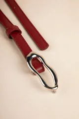 Cinturón fino color rojo de símil cuero con hebilla metálica irregular plateada.