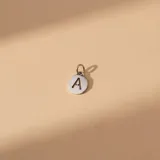 Dije circular de plata con letra inicial calada en el centro, incluye argolla para colgar.