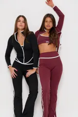 Conjunto deportivo de tres piezas compuesto por un top con breteles finos, una campera entallada con cierre frontal y una calza semioxford. Todas las prendas son de color negro con detalles de ribetes blancos en los bordes.