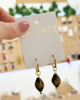 Par de aros colgantes con aro dorado y dije de piedra facetada color marrón.