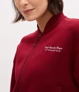 Campera deportiva tipo bomber de color bordó, con cierre frontal por cremallera, cuello redondo, mangas largas con puños elásticos y bolsillos laterales. Presenta un detalle de lettering bordado en el pecho.