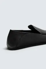 Mocasín de cuero negro, de estilo clásico y minimalista, con suela fina y horma cuadrada.
