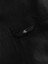Camisa negra de manga larga Calvin Klein Jeans confeccionada en tejido texturizado de algodón. Presenta cuello camisero, cierre con botones, bolsillo en el pecho con insignia del logo de la marca y puños con botones.