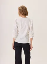 Remera de manga larga color negro con cuello en V y puños fruncidos. Presenta un estampado sutil en tonos grises y blancos en el centro del pecho, simulando un ramillete de flores secas.