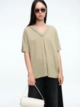 Remera de corte holgado y silueta cómoda, con escote en V y mangas cortas. Presenta costuras visibles en el cuello y los hombros, con un diseño minimalista y versátil.