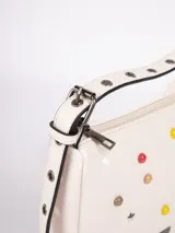 Cartera bandolera color crema de símil cuero, con apliques frontales de tachas redondas de colores y estrellas plateadas. Tiene correa regulable con hebillas y cierre superior con cremallera.