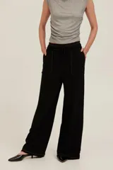 Pantalón negro de felpa ligera con tiro alto, corte relajado y pernera ancha. Cuenta con cintura elástica con cordón ajustable, bolsillos delanteros amplios con bordes sin rematar y detalles de costuras visibles.