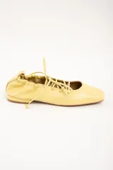 Chatitas de cuero color amarillo, con diseño acordonado en el empeine, puntera cuadrada y talón fruncido con cordón ajustable.