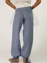 Pantalón de lino color beige, de corte holgado tipo jogger con puños ajustables con cintas en los tobillos, bolsillos laterales y cierre frontal con botón y cremallera.