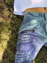 Pantalon de tiro medio y corte recto, confeccionado en tela con textura marcada y acabado rustico. Presenta un estampado artesanal con variaciones de tonos tierra y marrones, evocando un aspecto desgastado y natural.