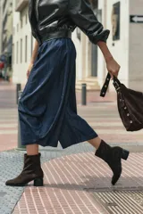 Bota de caña media confeccionada en cuero vacuno negro, con diseño minimalista y cierre trasero. Presenta un taco cilíndrico de madera tallada y punta cuadrada.