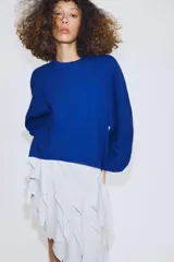 Jersey de punto color azul, con cuello redondo, mangas largas amplias y costuras marcadas en el frente.