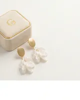 Caravanas de acero con baño de oro, compuestas por un disco superior metálico y un dije inferior con pétalos de resina blanca en forma de flor.