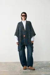 Ruana tejida en lana con diseño de trama en tonos azul y marrón, con detalle de flecos en el ruedo y parche de cuero en el frente.
