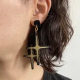 Aros colgantes con base cuadrada negra y dije con forma de estrella negra con interior dorado.