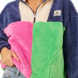 Buzo de polar con cierre frontal parcial y cuello alto. Presenta un diseño de bloques de color que combina azul marino, beige, fucsia y verde. Cuenta con bolsillos laterales y etiqueta de la marca en el pecho.