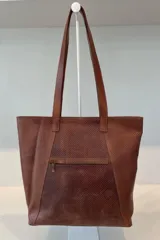 Bolso grande tipo tote color beige con textura tejida y costuras decorativas en los laterales. Tiene doble asa de hombro y logo de la marca en el frente. Interior forrado con bolsillo con cierre y portacelular.