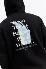 Campera negra con capucha y cierre frontal, confeccionada en algodón. Presenta un diseño gráfico en la espalda con la frase 'Good Things Happen When You Try' sobre un trazo de pintura en tonos pasteles y el logo de la marca Mistral.