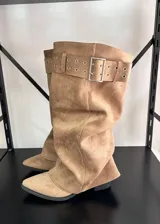 Botas altas de gamuza color beige, con diseño slouchy, punta fina y una tira ancha superior con hebilla metálica rectangular y ojalillos.