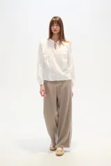 Blusa blanca de algodón con volados frontales, cuello redondo con lazo ajustable y mangas largas abullonadas con puños elásticos.