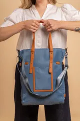 Bolso tipo tote bag de símil cuero color rosa pálido, con asas dobles y detalles de costura en color beige claro. Presenta un bolsillo frontal rectangular aplicado y herrajes metálicos.