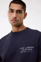 Remera de algodón color gris oscuro con cuello redondo y estampado pequeño en el pecho con texto en color blanco.