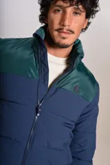 Campera puffer con diseño bicolor, cuerpo en azul marino y canesú superior en verde oscuro. Presenta cuello alto, cierre frontal completo y puños elásticos.