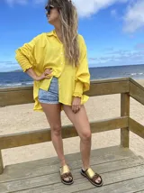 Camisa amarilla de lino, corte oversize, con cuello clásico, cierre frontal con botones y mangas largas con puños elastizados.