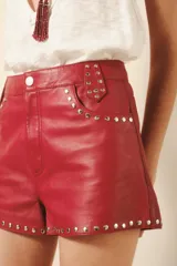 Short de cuero ovino negro con remaches metálicos plateados en presillas, bolsillos y ruedo. Presenta un lavado con efecto arrugado y cierre frontal de cordones.