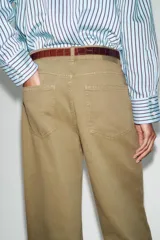 Jeans de tiro alto color azul oscuro, con cinco bolsillos, pernera ancha y nervio marcado en el delantero. Incluye un cinturón fino de cuero sintético marrón con textura de cocodrilo. Cierre frontal con cremallera y botón.