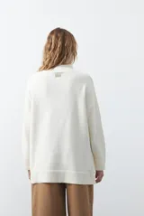 Polera de tejido de punto color marrón, con diseño asimétrico y costura diagonal frontal. Presenta cuello alto, hombros caídos, mangas largas con puños acanalados y ruedo con abertura frontal.