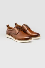 Zapato de cuero marrón tipo derby, con cordones oscuros y suela blanca estilo deportivo.