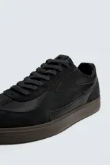 Zapatilla deportiva de estilo retro con diseño de paneles combinados en tonos beige y crema. Presenta detalles en gamuza y una suela de goma en color caramelo.