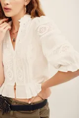 Camisa blanca de algodón con detalles de encaje broderie y transparencias, escote en V con cuello alto con volados, y mangas cortas abullonadas.