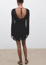 Vestido corto de crochet negro con cuello redondo y mangas largas acampanadas. Presenta una espalda abierta con cierre de lazo y cuenta con forro interior.