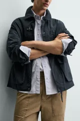 Parka de corte relajado confeccionada en mezcla de algodón color marrón. Presenta cuello solapa, cierre frontal con cremallera oculta y alamares metálicos, bolsillos de plastrón con solapa en la cadera y bolsillo de vivo en el pecho.