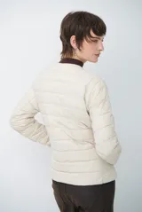 Campera acolchada tipo puffer en color beige, con diseño sin cuello y cierre frontal con botones a presión.