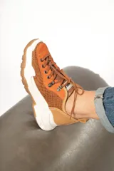 Zapatillas urbanas color óxido, con cordones marrones, suela gruesa blanca y detalles en cuero texturizado.