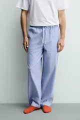 Set de pijama para hombre compuesto por una remera blanca de cuello redondo y mangas cortas, y un pantalón celeste a rayas verticales con cintura elástica y bolsillos laterales.