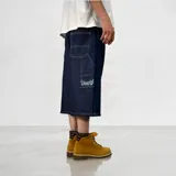 Bermuda de jean estilo baggy, confeccionada en denim de algodón premium con textura rústica. Presenta un diseño de corte amplio, costuras reforzadas en contraste y un bordado distintivo en la parte inferior de la pierna.