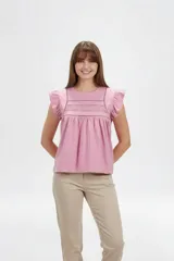 Remera de algodón color rosado, de corte holgado y mangas cortas con volados, con detalle de encaje en el frente y cuello redondo a la base.