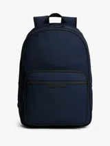 Mochila de poliéster color azul marino con ribetes negros. Presenta un diseño liso, asa superior, correas ajustables y acolchadas, y un panel trasero de malla acolchado. Cuenta con un compartimento principal amplio, funda para portátil incorporada, bolsillo interior con cremallera y bolsillo exterior con cremallera, donde se ubica el logo metálico de Tommy Hilfiger.
