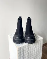 Botas cortas de cuero vacuno color negro, con diseño combinado de gamuza y cuero texturizado con efecto reptil en el talón. Presentan cierre lateral metálico, puntera reforzada y suela track dentada con costura visible.